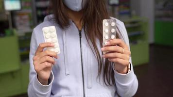 Woman wearing a mask holds and show medication at pharmacy video