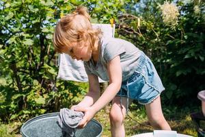 la niña de preescolar ayuda con la lavandería. niño lava ropa en el jardín foto