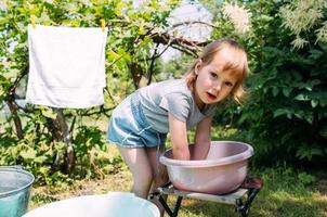 la niña de preescolar ayuda con la lavandería. niño lava ropa en el jardín foto