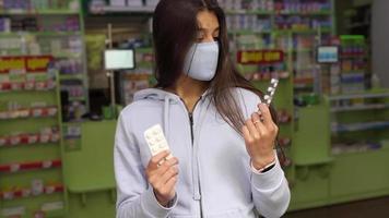 Woman wearing a mask holds and show medication at pharmacy video