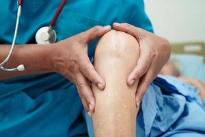 Doctor checking Asian elderly woman patient with scar knee replacement surgery in hospital. photo