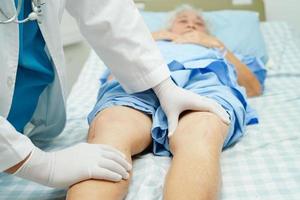 Doctor checking Asian elderly woman patient with scar knee replacement surgery in hospital. photo