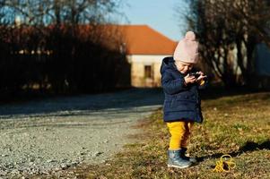 Little baby girl in the sunny day hold mobile phone in hands. photo