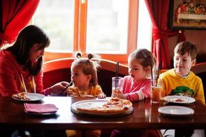 Children on birthdays sitting at the table and eating pizza. photo