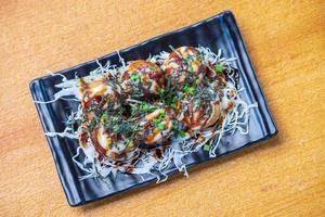 Octopus Fillet Takoyaki Garnish with seaweed. chopped white cabbage and scallions in a black dish, Saimoden, circled on a wooden table photo