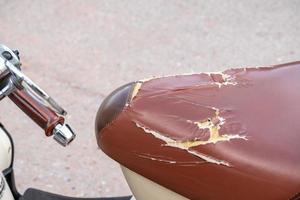 The red-brown motorcycle seat is damaged. due to use and not being properly maintained, motocycle broken seat photo