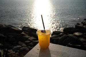 taza de jugo de naranja en la mesa superior junto al mar durante la luz del día del cielo del atardecer. foto