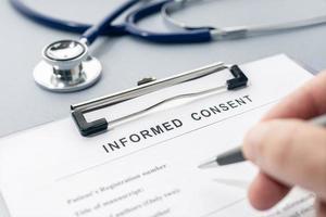 Hand filling a Informed Consent form and stethoscope on desk photo
