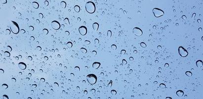 Perspectiva de gotas de agua a través de la superficie de cristal de la ventana contra el cielo azul bueno para contenido multimedia foto