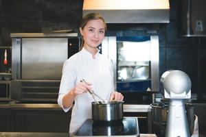 Portrait of confident and smiling young woman chef dressed in white uniform, professional kitchen are on background photo