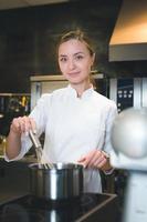 Portrait of confident and smiling young woman chef dressed in white uniform, professional kitchen are on background photo