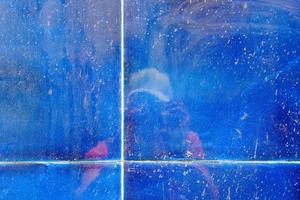 Reflection of a person with a photo camera in the blue liquid ceramic tile wall, abstract background, grunge texture and pattern.