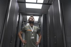 Portrait of male technician or network administrator standing brave as a hero with arms crossed in data center server room. photo