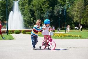 niño y niña en el parque aprendiendo a andar en bicicleta foto