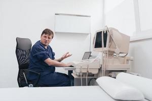 Orthopedist doctor examining X-ray picture at desk in clinic on laptop computer photo