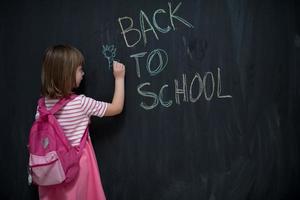school girl child with backpack writing  chalkboard photo