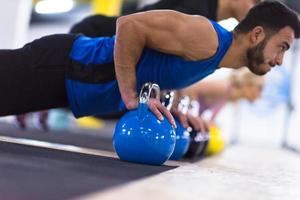 atletas jóvenes haciendo flexiones con pesas rusas foto