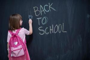 school girl child with backpack writing  chalkboard photo