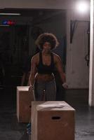 black female athlete is performing box jumps at gym photo