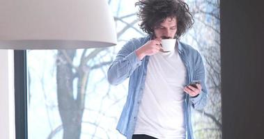 joven bebiendo café y usando un teléfono móvil en casa foto