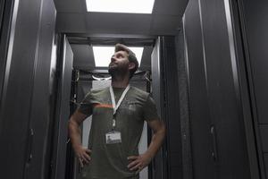 Portrait of male technician or network administrator standing brave as a hero with arms crossed in data center server room. photo