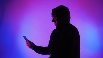 Anonymous hacker and face mask with smartphone in hand. photo