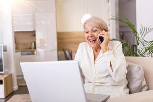 Senior woman receiving good news on phone. screaming out of happiness. Mature excited woman screaming in happiness while talking on a phone and using laptop photo