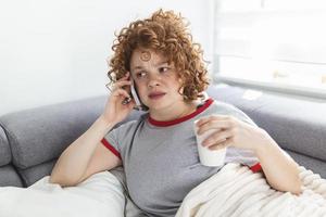 Young woman getting bad news by phone. unhappy woman talking on mobile phone looking down. Crying depressed girl holds phone sitting on sofa hopeless , breaking up, scared of threatening, mobile abuse photo