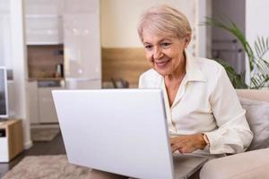 Happy senior woman making online payments of bill using laptop. Smiling mature woman shopping online. Pensioner using laptop for internet banking photo