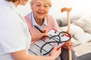 Senior woman is visited by her doctor or caregiver. Female doctor or nurse talking with senior patient. Medicine, age, health care and home care concept. Senior woman with her caregiver at home photo