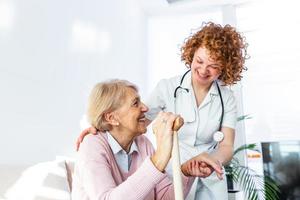 Friendly relationship between smiling caregiver in uniform and happy elderly woman. Supportive young nurse looking at senior woman. Young caring lovely caregiver and happy ward photo