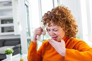 Sick desperate woman has flu. Rhinitis, cold, sickness, allergy concept. Pretty sick woman has runnning nose, rubs nose with handkerchief. Sneezing female. Brunette sneezing in a tissue
