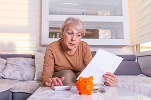 Senior old woman shocked with the bills she receives, appalled and gasping. tressed Senior woman checking finance with calculator at home. Retired woman calculating her domestic bills photo