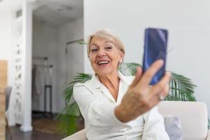 abuela tomando selfies en casa en la sala de estar. primer plano retrato de feliz alegre encantadora encantadora hermosa anciana abuela abuela tomando un selfie. concepto de vejez, jubilación y personas foto