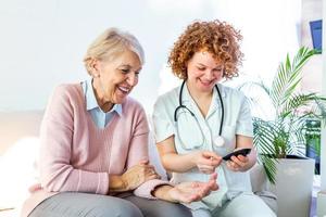 Happy senior woman having her blood sugar measured in a nursing home by her caregiver. Happy nurse measuring blood sugar of a senior woman in living room - diabetes and glicemia concept photo