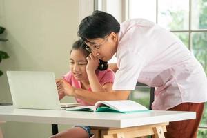 Father is teaching his daughter to do homework during online distance learning at home. photo