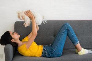 bella mujer jugando con un perro shihtzu en un sofá en casa foto