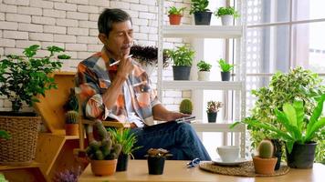 An old man sitting in a living room decorated with flower pots. photo