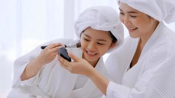 Mother with little daughter in bathrobes doing beauty treatment together in bedroom. photo