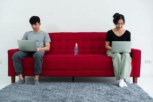 Happy Asian couple with sanitizer alcohol gel while sitting working together on sofa at home. photo