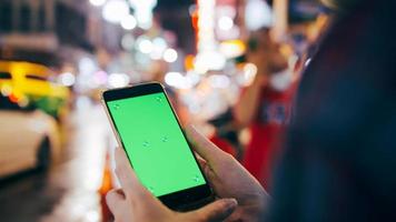 mujer turista sosteniendo un teléfono inteligente con pantalla verde mientras está de pie en la calle por la noche. foto