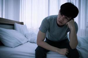 Stressed Asian young man sitting alone on bed. Bad relationship or bankrupt problem and sickness concept. photo