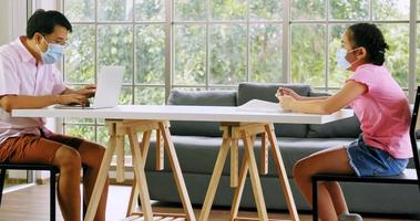 Father and daughter wear protective masks and keep the social distance while working at home. photo