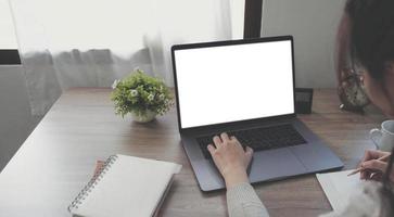 imagen de una mujer que usa y escribe en una computadora portátil con una pantalla de escritorio en blanco en una mesa de madera foto