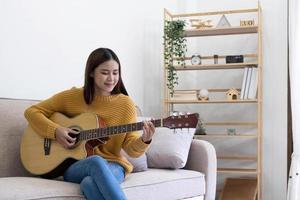 mujer joven inspirada componiendo canciones en guitarra acústica en casa foto