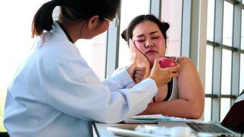 Female doctor suggesting unhappy chubby woman to eat apple in hospital room. photo