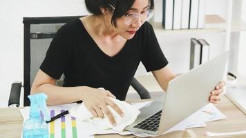 Young woman cleaning the surface of laptop with alcohol spray and fabric at home photo