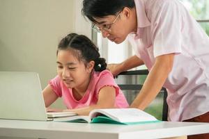 Father is teaching his daughter to do homework during online distance learning at home. photo