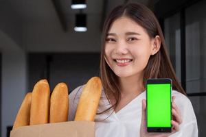 mujer feliz sosteniendo pan recién horneado y teléfono inteligente, concepto de entrega de alimentos foto