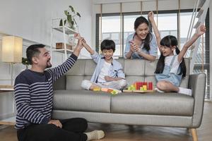 Happy Asian lovely Thai family care, dad, mum, and little children have fun playing with colorful toy blocks together on sofa in white living room, leisure weekend, and domestic wellbeing lifestyle. photo